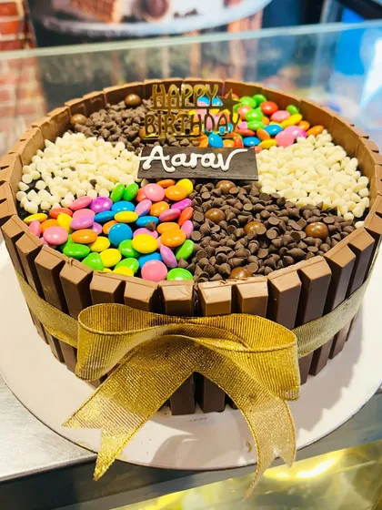 A fun KitKat cake with a gold ribbon, the top divided into four sections filled with gems, chocolate chips, and white chocolate chips.