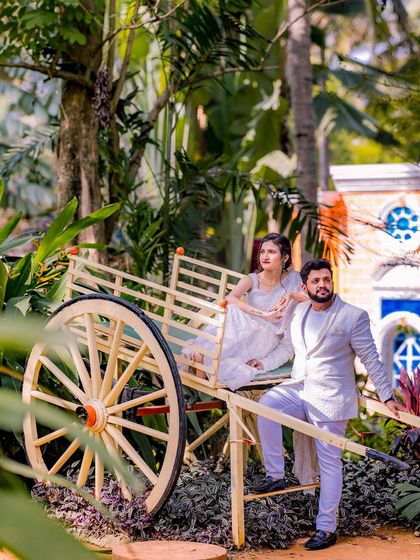 A couple with a rustic bullock cart prop, adding a touch of rural charm to the garden setting.