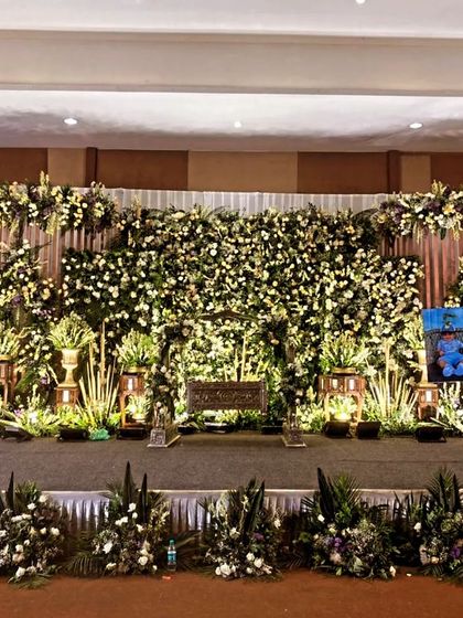 A stage with a white floral wall and lush green arrangements.