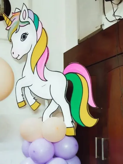 A full-body unicorn cutout with a rainbow mane, standing on a pastel balloon pillar.