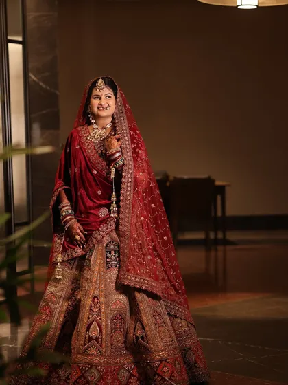 A full-length portrait of the bride. The overall look is regal and timeless, with makeup that complements her stunning velvet lehenga.