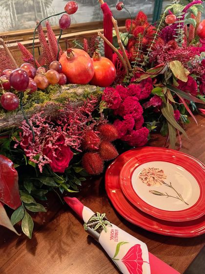 A beautiful composition showing the relationship between the place setting and the centerpiece. The colors of the plate and napkin are echoed in the pomegranates, grapes, and flowers of the table runner.