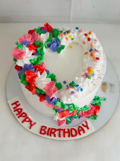 A vibrant floral heart cake, with one half made of colorful buttercream flowers and the other of sprinkles.