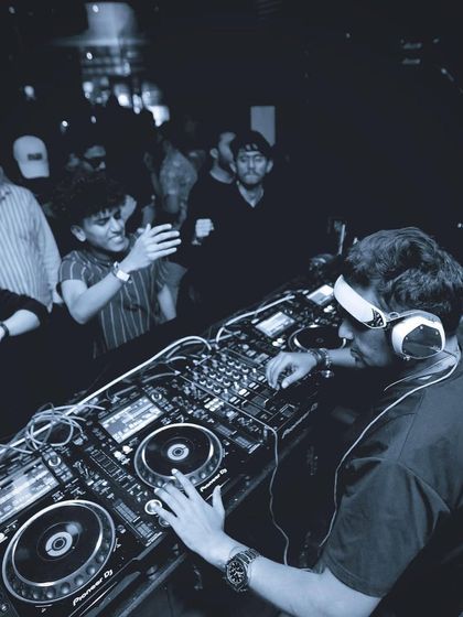 A blue-tinted, moody shot from behind the decks. The focus is on the intricate details of the mixer and the craft of DJing.