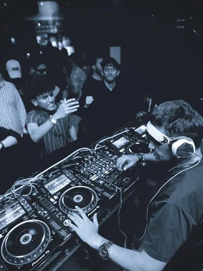 A blue-tinted, moody shot from behind the decks. The focus is on the intricate details of the mixer and the craft of DJing.