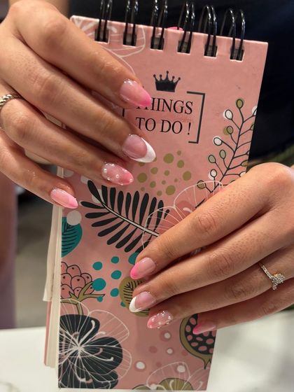 A soft and pretty pink and white French manicure on almond-shaped nails, with a subtle glitter accent for a touch of sparkle.