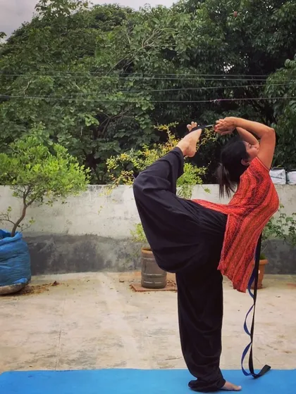 Practicing Natarajasana (Dancer's Pose) on my terrace with a strap. The strap helps me get a better grip and deepen the backbend without compromising my alignment.