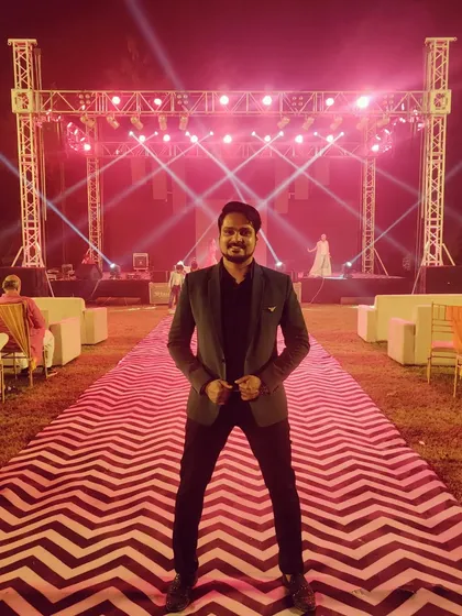 A full shot of my Sangeet look against the grand stage setup. A well-dressed anchor adds to the overall visual appeal of the event.