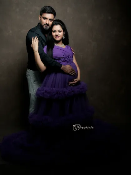 A romantic studio portrait of a couple, with the mother-to-be in a purple ruffled gown.
