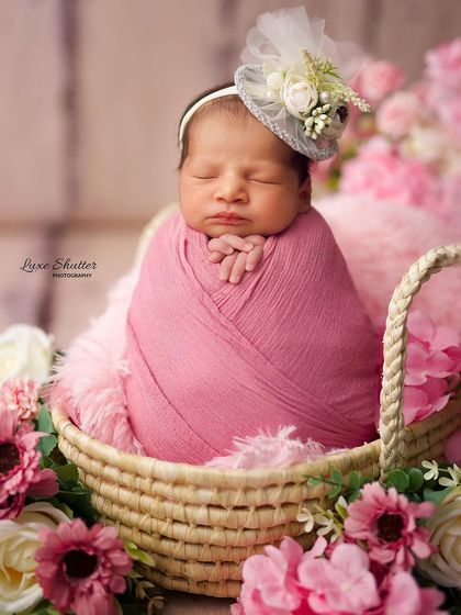 A close-up of the sleeping baby in her pink floral basket, wearing an adorable little fascinator hat.
