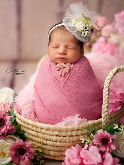 A close-up of the sleeping baby in her pink floral basket, wearing an adorable little fascinator hat.