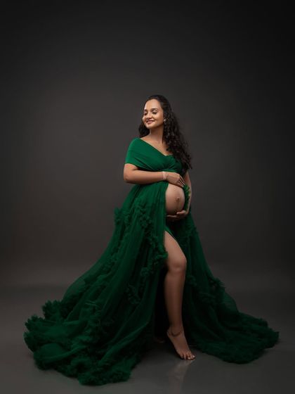 The full, dramatic sweep of the emerald green gown. This shot captures the grandeur of the dress and the radiant confidence of the mother-to-be.