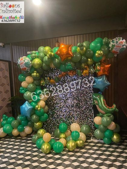 A dinosaur themed party with a silver shimmer backdrop and a garland of green balloons, perfect for a prehistoric adventure.