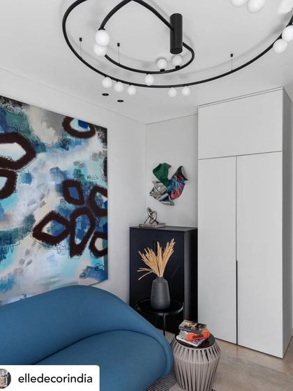 This family room corner features a vibrant blue sofa and a large abstract painting. The sculptural ceiling light and minimalist wardrobe ensure that the focus remains on the powerful combination of color and art.