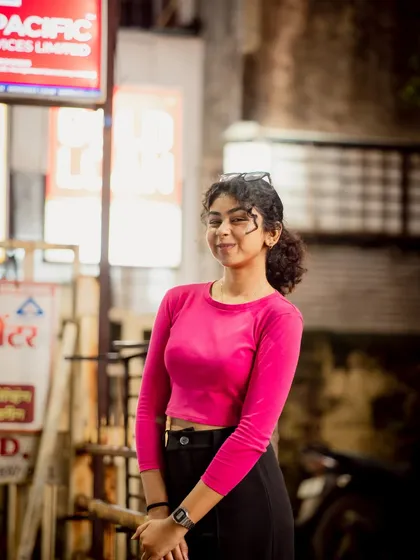 A candid-style night portrait on a city street. The bright pink top stands out beautifully against the darker, neutral background.