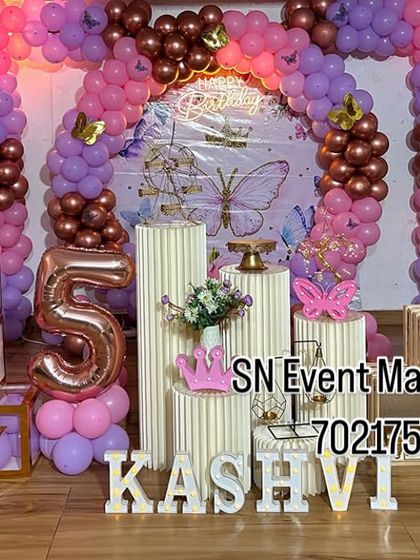 An elegant butterfly setup with beautiful props. This decoration includes tiered stands, "BABY" blocks, a picket fence, and a lovely balloon arch in pink, purple, and rose gold.