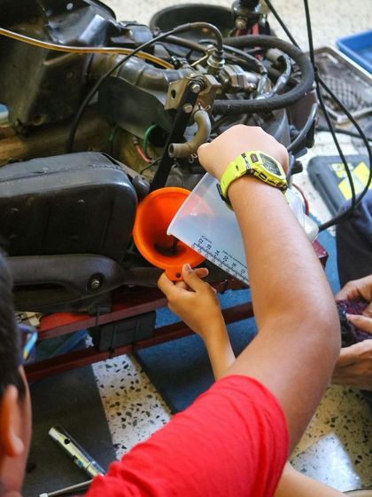 A student carefully uses a funnel to add oil to the engine during our motorcycle servicing session. They are learning a real-world skill that combines measurement, mechanics, and responsibility.