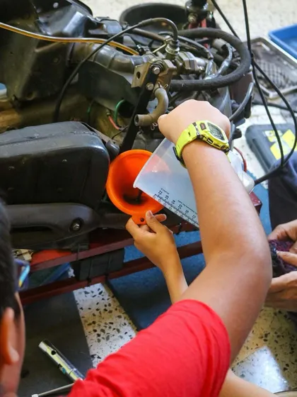 A student carefully uses a funnel to add oil to the engine during our motorcycle servicing session. They are learning a real-world skill that combines measurement, mechanics, and responsibility.