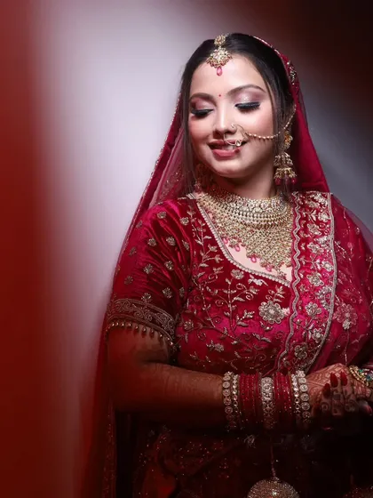 A soft and gentle portrait of the bride in a red velvet lehenga. The lighting is focused to create a classic, painterly effect.