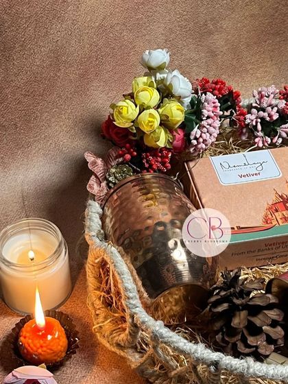 Our exclusive Diwali hampers are crafted with love for your work family. This jute basket is filled with a copper tumbler, a candle jar, and other festive treats, decorated with lights and flowers.
