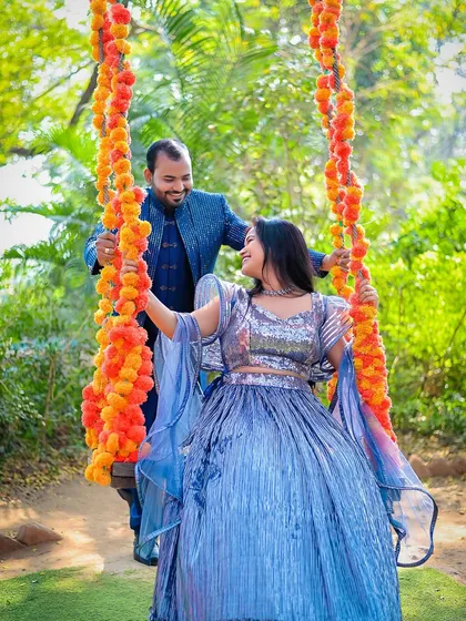A joyful pre-wedding shot of a couple on a swing decorated with marigold flowers. The groom pushes the swing as they share a happy glance, perfectly capturing a moment of shared fun and affection.