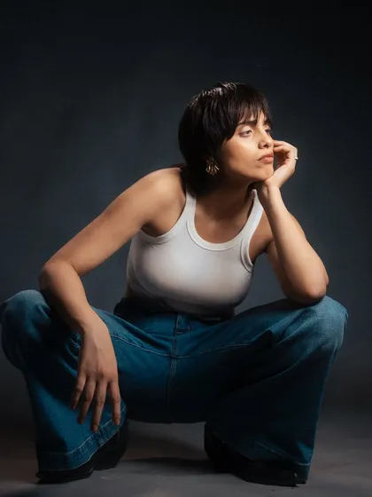 A thoughtful and composed portrait. The low-angle squat and pensive expression, combined with the dark background, create a cinematic and introspective mood.