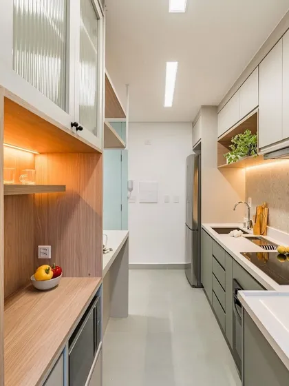 A galley kitchen designed for maximum efficiency in a compact space. The light green and wood-tone cabinets, along with open shelving and under-cabinet lighting, make the area feel bright and functional.