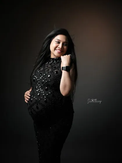 A joyful and candid shot of a mother-to-be in a black sequined gown. Her happy expression and the dynamic movement of her hair create a vibrant and glamorous portrait.