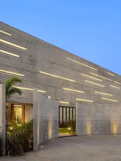 The entrance to the Laxcon office is framed by imposing, textured concrete walls that guide visitors into the main building. The facade's brutalist character is softened by integrated lighting and surrounding landscape design.
