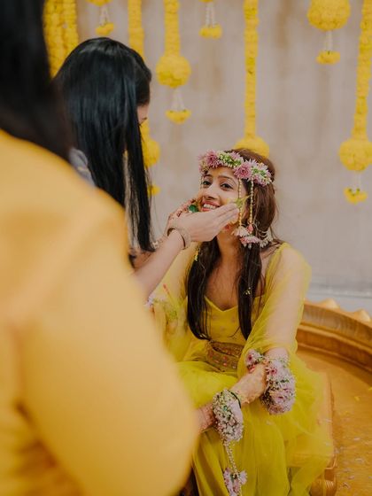 A tender moment as a friend gently applies Haldi to the bride's cheek, showcasing the love and support surrounding her.