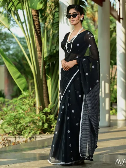 Another shot of the black handloom saree, this time with a focus on the full silhouette. The elegant drape of the saree is highlighted against the clean lines of the architecture.