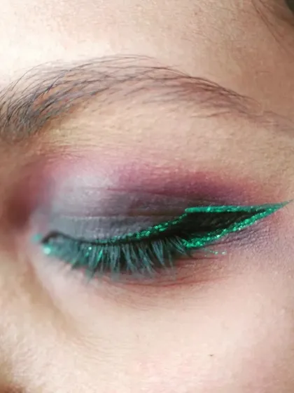 A close-up on a bold party eye makeup look. This demonstrates my skill in detailed application, featuring a purple smokey eye effect dramatically defined by a sharp, green glitter winged eyeliner. This is perfect for clients wanting a glamorous and striking look.