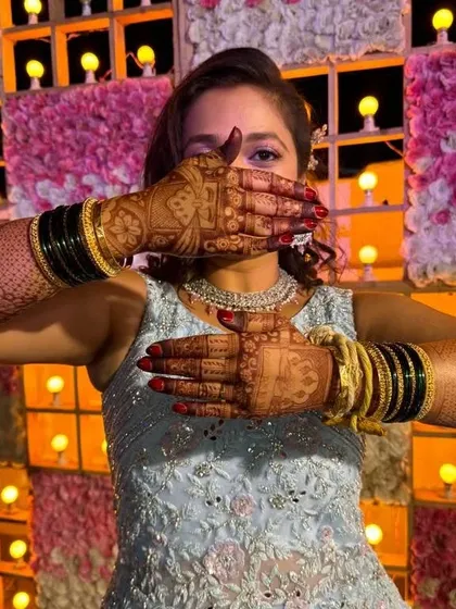 A happy bride showing off her beautifully stained hands against a festive background. The dark henna is the perfect accessory.