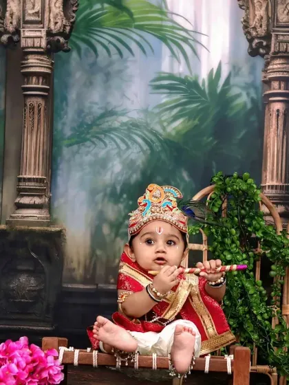 A sweet baby Krishna holds his flute, surrounded by a lush green backdrop with a peacock and temple pillars.