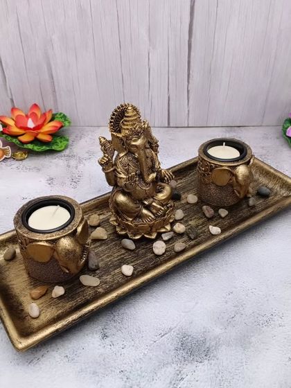 A decorative set featuring a Ganesha idol on a tray with two candle holders. This makes for a beautiful centerpiece or a thoughtful housewarming gift.
