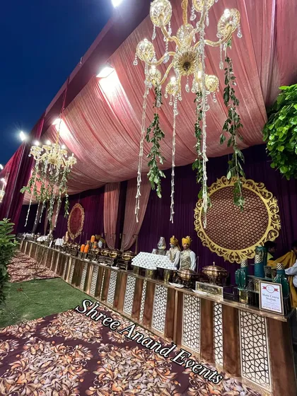 A grand catering setup under a canopy of chandeliers, with staff in traditional attire ready to serve the guests.
