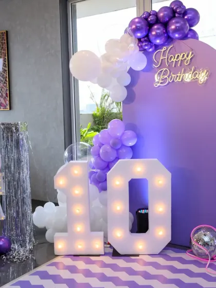 The full backdrop for the 'Wish' inspired 10th birthday party, featuring purple panels, marquee numbers, and a cascade of white and purple balloons.