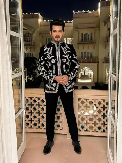 A stunning black Jodhpuri jacket with all-over silver floral embroidery, worn by a client against a beautiful backdrop. Ideal for a destination wedding.