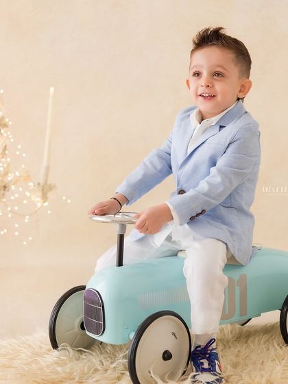 A little boy looking dapper in his suit, enjoying a ride on a vintage toy car. A classic and playful portrait.