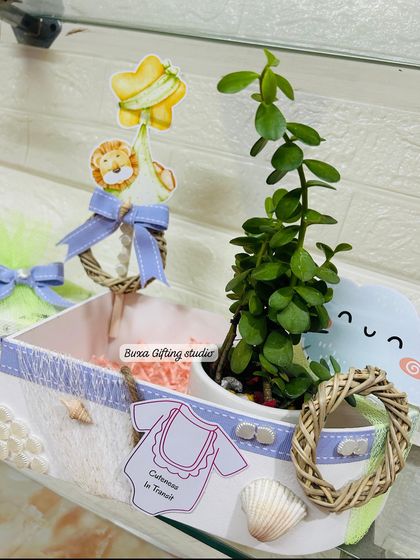 A detailed view of the boat-shaped baby shower hamper. I used a jade plant, lilac ribbons, and seashell accents to create a serene, nautical feel.