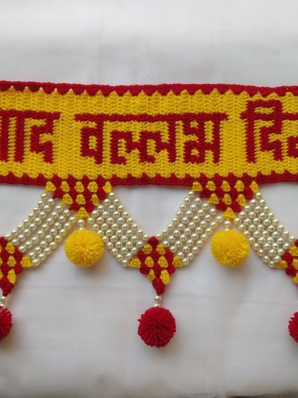 A close up of the "श्रीपाद वल्लभ दिगंबरा" text on a toran, showcasing the clarity of the crocheted letters in red against a yellow background.