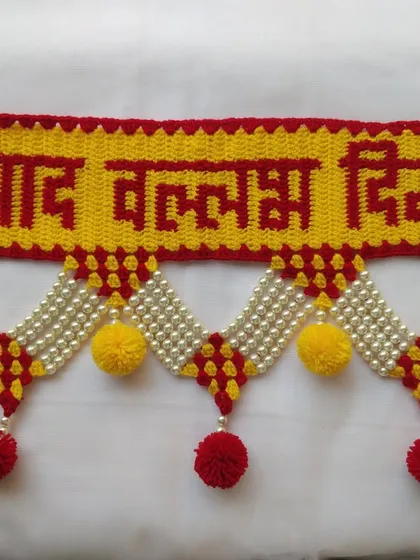 A close up of the "श्रीपाद वल्लभ दिगंबरा" text on a toran, showcasing the clarity of the crocheted letters in red against a yellow background.