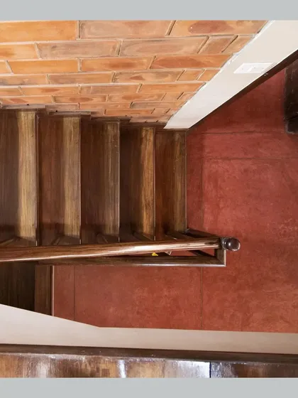 A top-down view of a wooden staircase against a red oxide floor, highlighting the rich textures and colors of the materials.