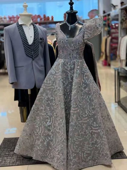 This grey embroidered ball gown, paired with a men's tuxedo, is perfect for a coordinated couple's look at a reception. The unique one-shoulder ruffle adds a high-fashion touch.