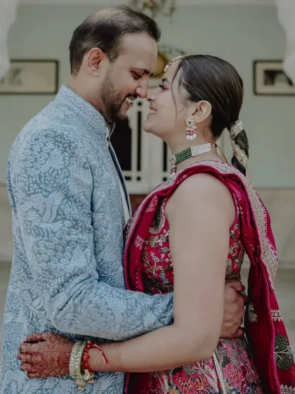 A joyful close-up of a couple sharing a loving gaze. The vibrant colors of the bride's pink and red lehenga and the groom's powder blue jacket create a festive and happy mood.