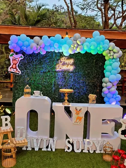 A simple yet charming animal theme setup for a first birthday, featuring large 'ONE' block letters and cute giraffe and zebra cutouts against a grass wall.