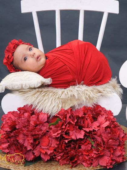 A full view of the setup, showing the baby on the chair with a bed of red flowers at the base. The contrast between the white, red, and dark grey is lovely.