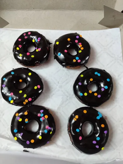 A simple box of six classic round donuts. Each one is hand-dipped in a glossy chocolate glaze and topped with a light scattering of colorful sprinkles.