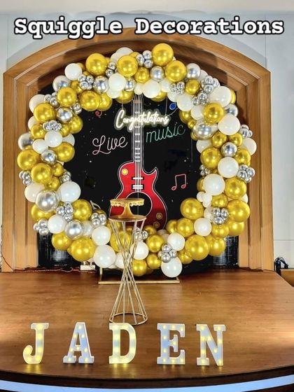 A music-themed decoration for a Confirmation ceremony. The design includes a guitar cutout, a 'Congratulations' neon sign, and a gold, white, and silver balloon ring.