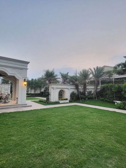 A view across the lawn towards a classical gazebo at a Gurugram farmhouse. The composition of open green space and elegant structures creates a balanced and stately landscape.